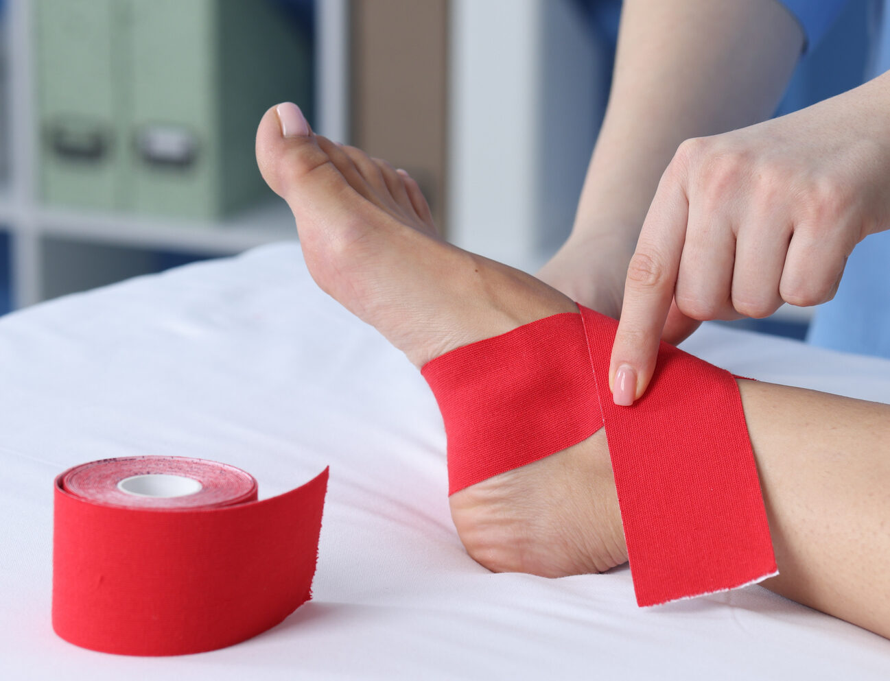 Doctor applying kinesio tapes to patient’s foot in hospital, closeup
